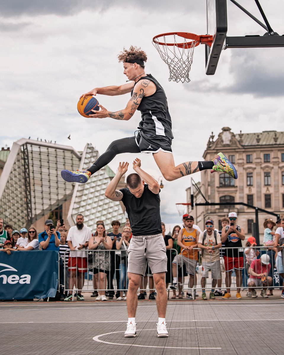 Konkurs wsadów podczas Enea Basket na Wolności 2026, fot. Klaudia Berda/ Enea Basket na Wolności - zawodnik z piłką przeskakuje nad innym koszykarzem z pilką w rękach i próbuje zrobić wsad do kosza