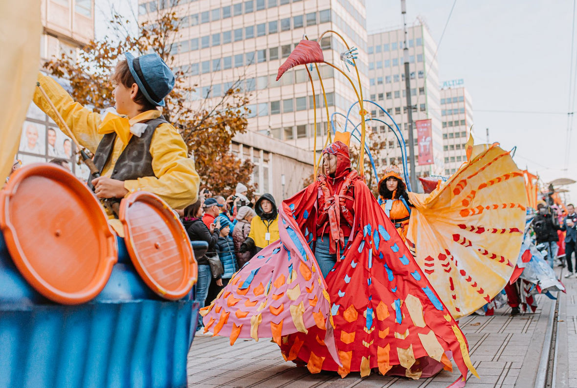 korowód idący przez ulicę w korowodzie osoby w barwnych strojach wzdłuż ulicy ustawieni ludzie oglądający korowód