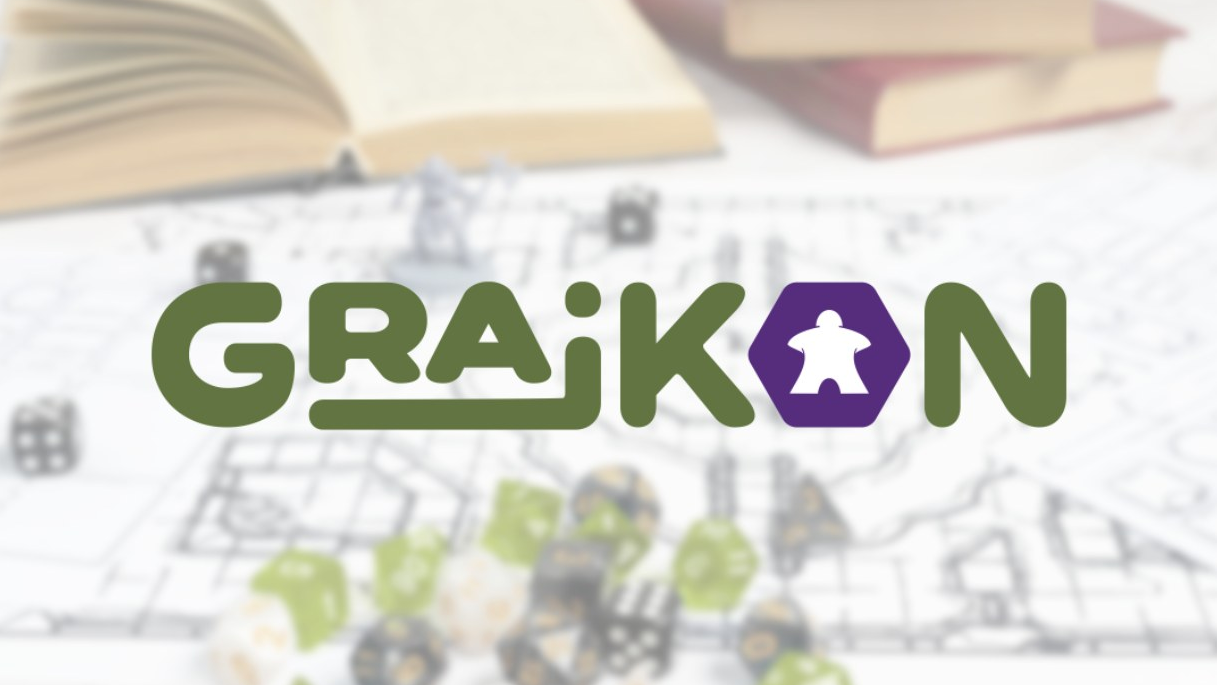 Logo wydarzenia "GRAJKON" na jasnym, rozmytym tle przedstawiającym elementy gier planszowych. Napis wykonany jest grubą, zieloną czcionką, przy czym litera "O" ma kształt fioletowego sześciokąta z białą sylwetką pionka typu meeple w środku. W tle widoczne są zarysy otwartej książki, kości do gry oraz planszy.