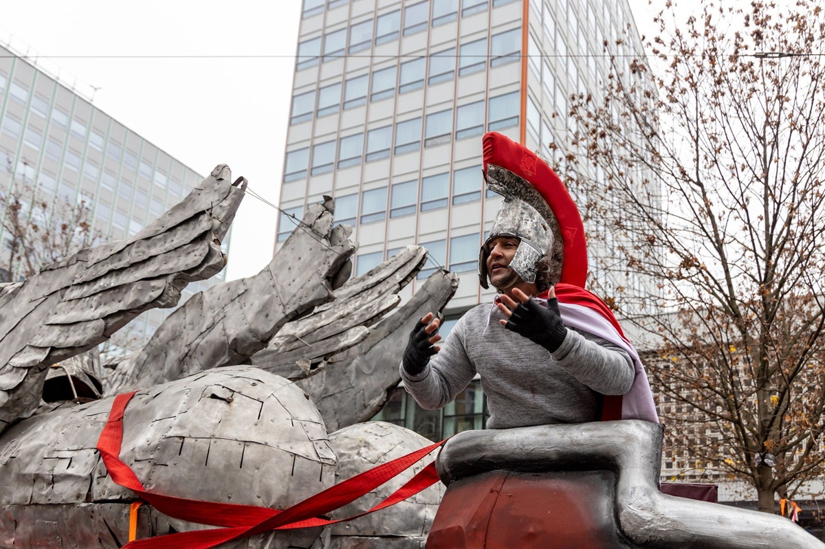 mężczyzna w stroju rzymskiego legionisty podczas korowodu świętomarcińskiego jest na podwyższeniu za nim widać fragment wieżowców przy ulicy