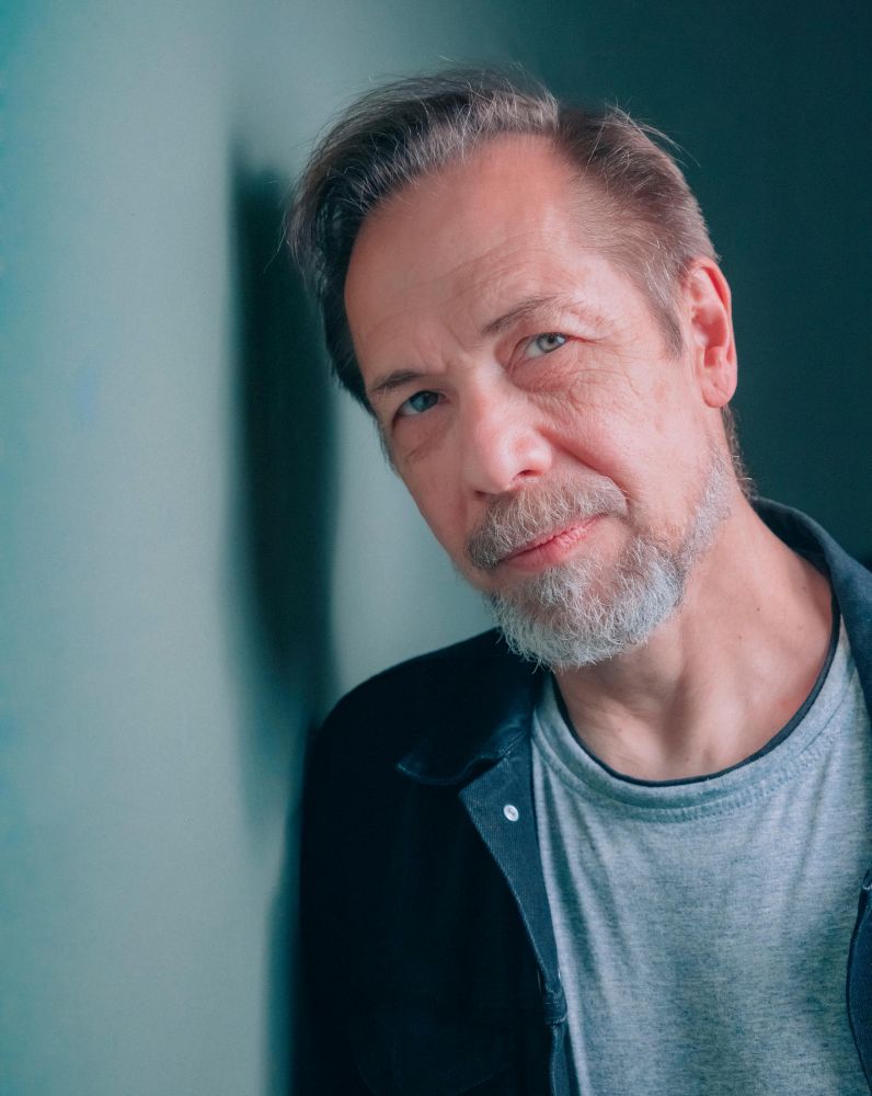 Mężczyzna z brodą opiera głowę o ścianę.