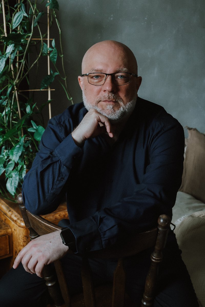 Mężczyzna z siwą brodą i w okularach podpiera brodę ręką