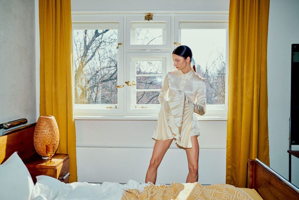 Młoda dziewczyna w białej koszuli stoi na tle okna.