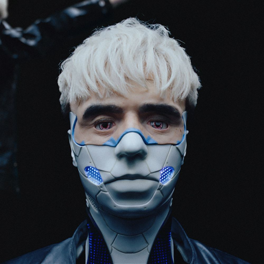 Młody mężczyzna w blond włosach z plastikową maską na dolnej połowie twarzy.