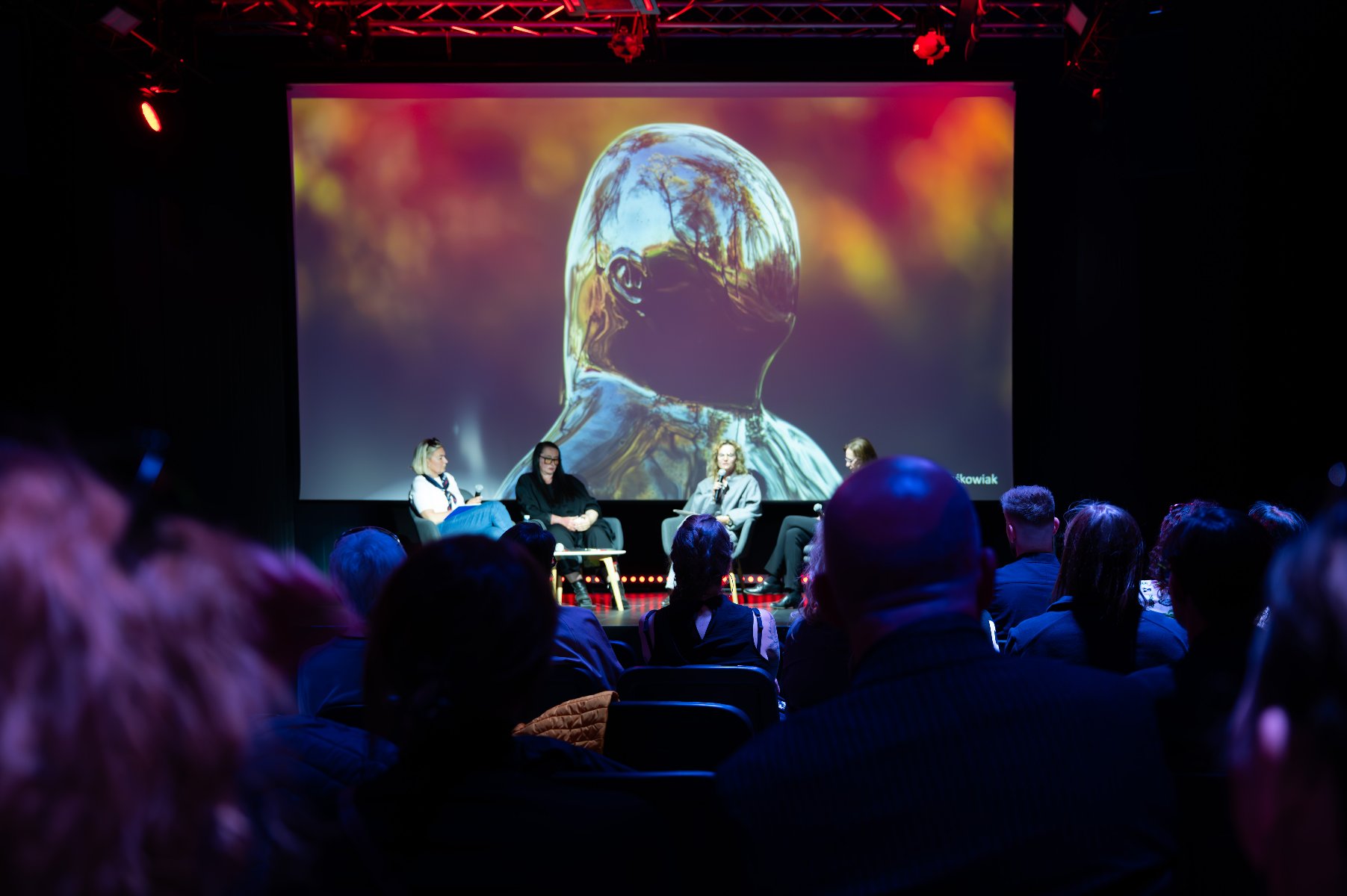 Na scenie siedzą cztery kobiety. Sala w ciemnych kolorach.