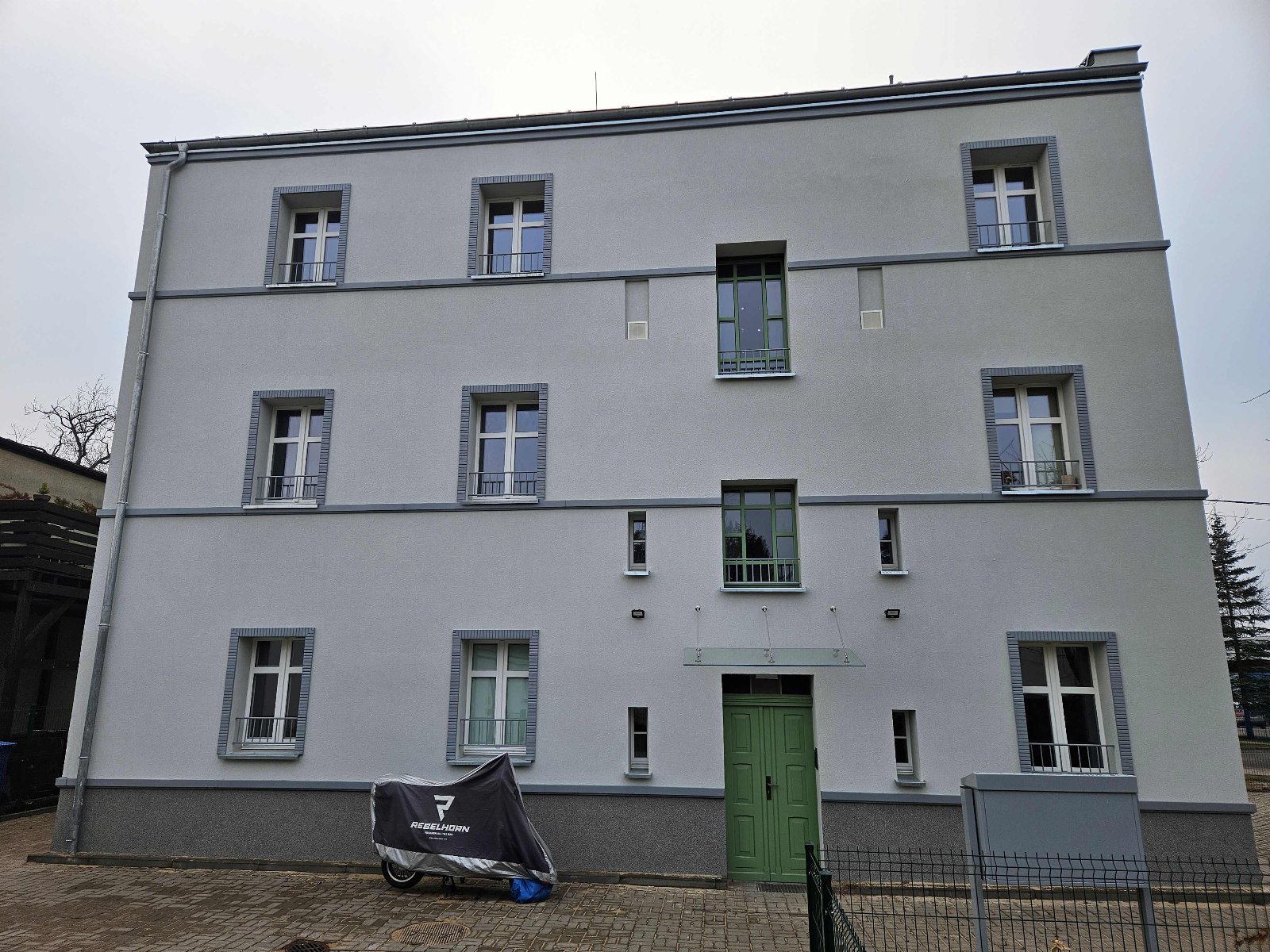 Na zdjęciu biały budynek w otoczeniu drzew