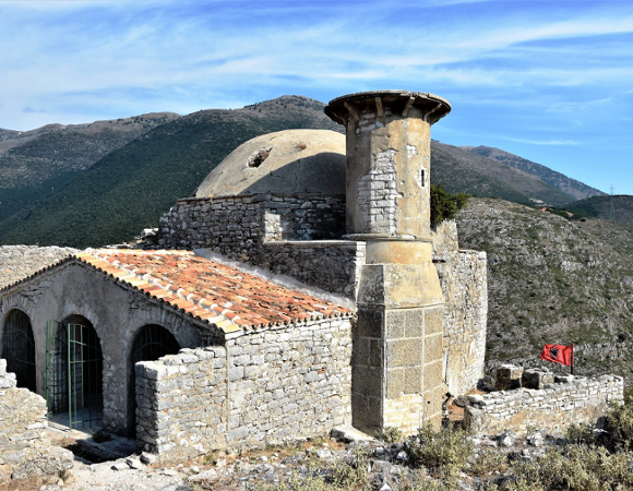Na zdjęciu budowla wśród gór, na niej widać flagę Albanii