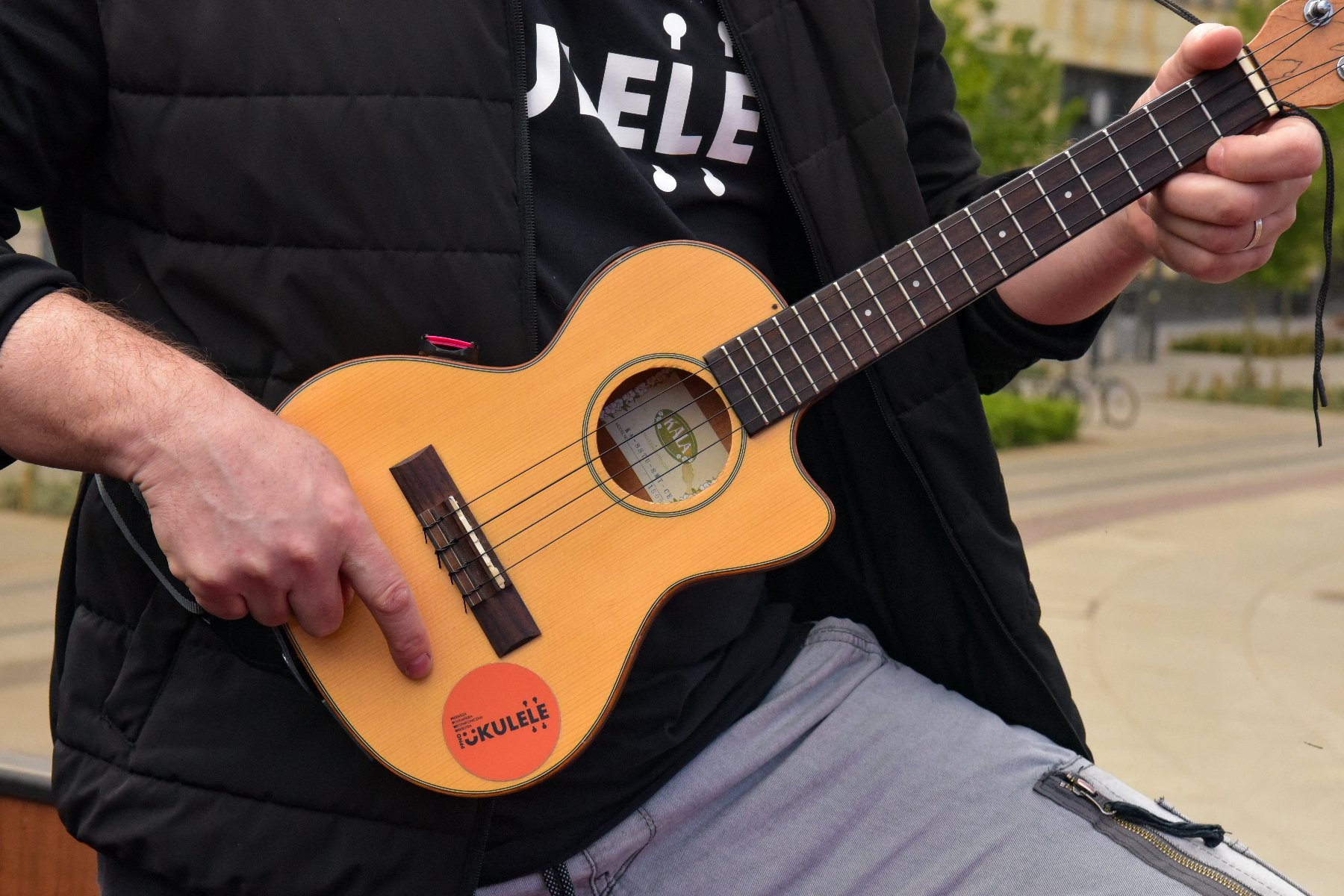 Na zdjęciu człowiek grający na ukulele, widać tylko jego dłonie