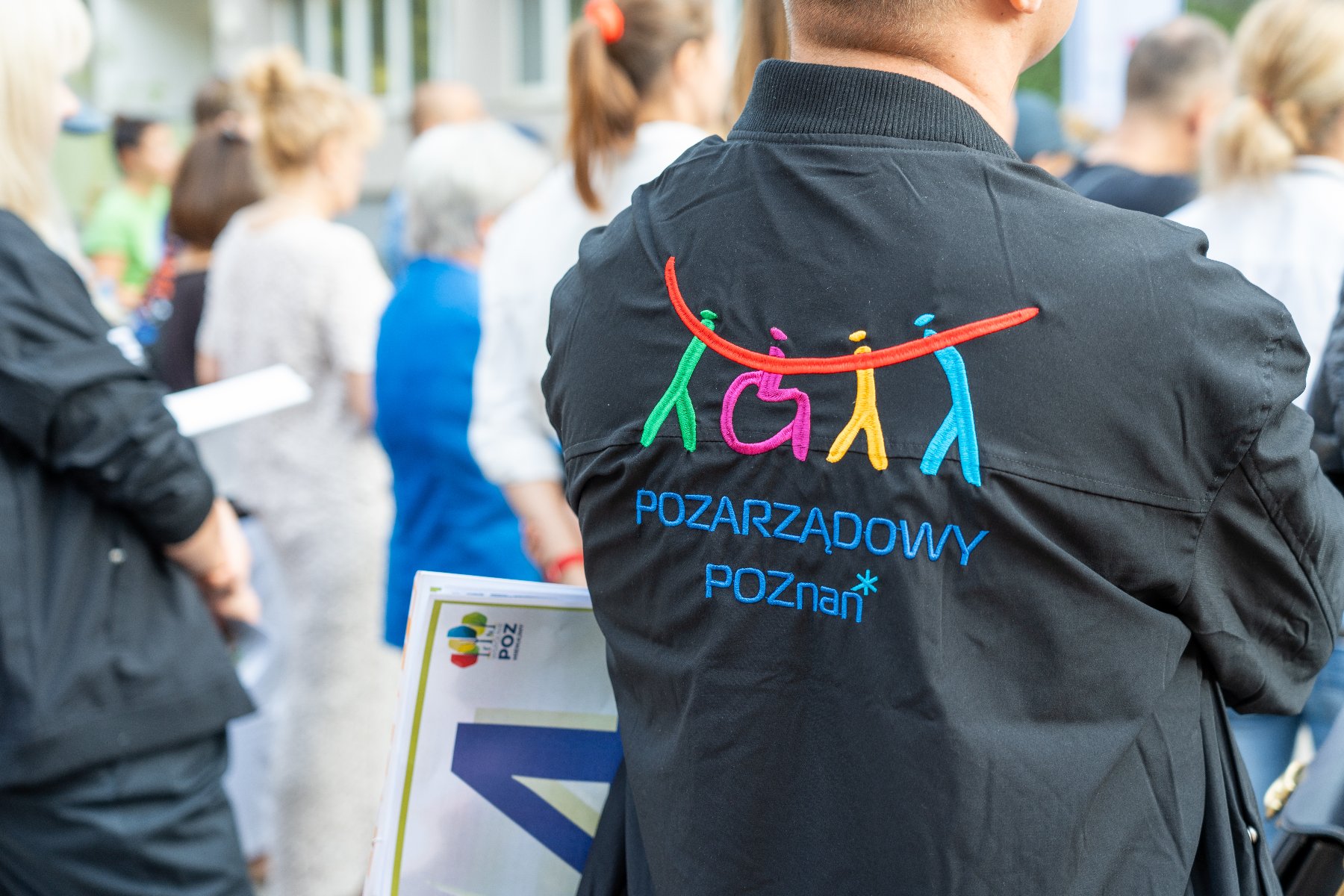Na zdjęciu człowiek w kurtce z napisem: pozarządowy Poznań, stojący tyłem do obiektywu
