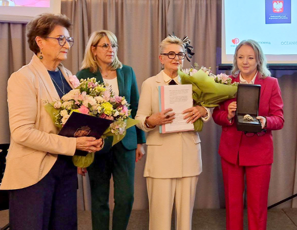 Na zdjęciu cztery kobiety, jedna z nich trzyma srebrną pieczęć, inne - kwiaty