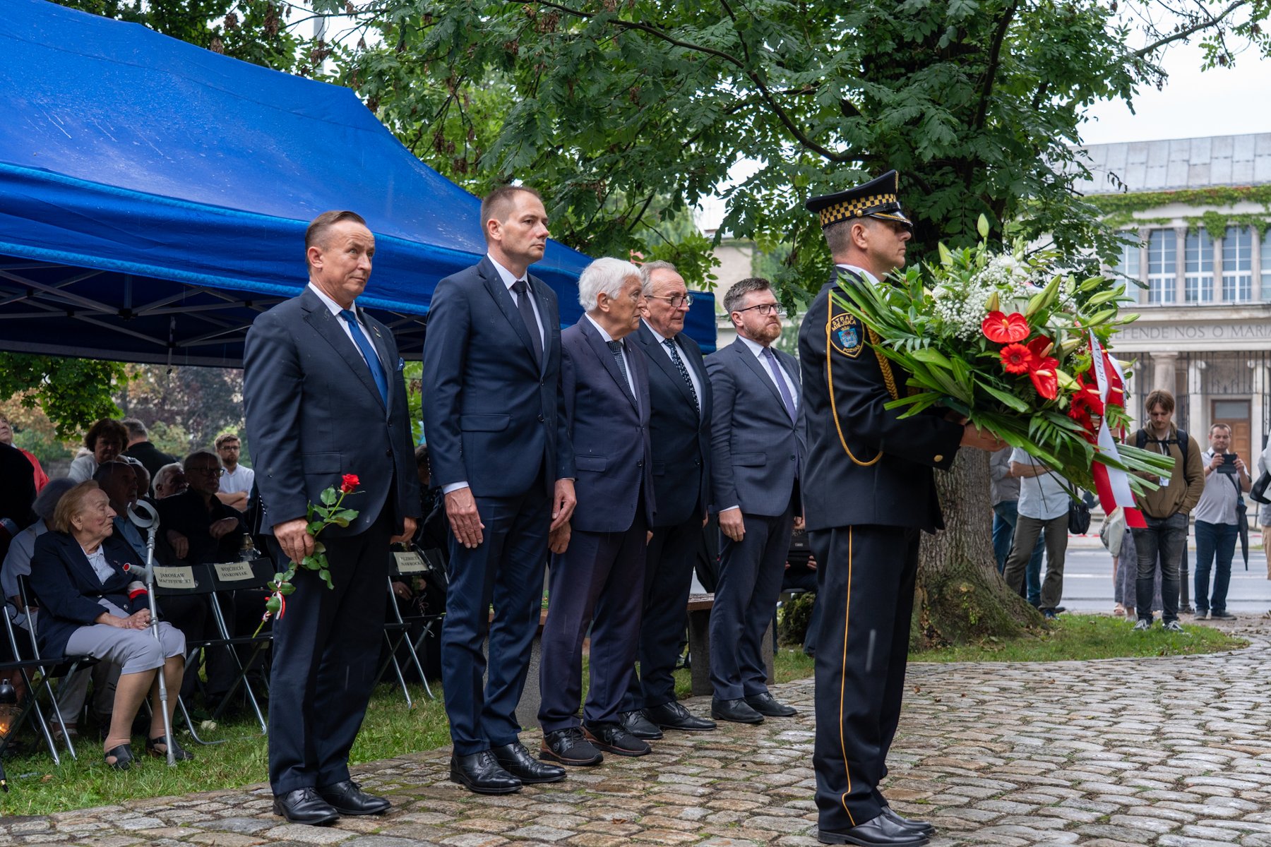 Na zdjęciu delegacja do składania kwiatów, przed nią strażnik miejski z wiązanką