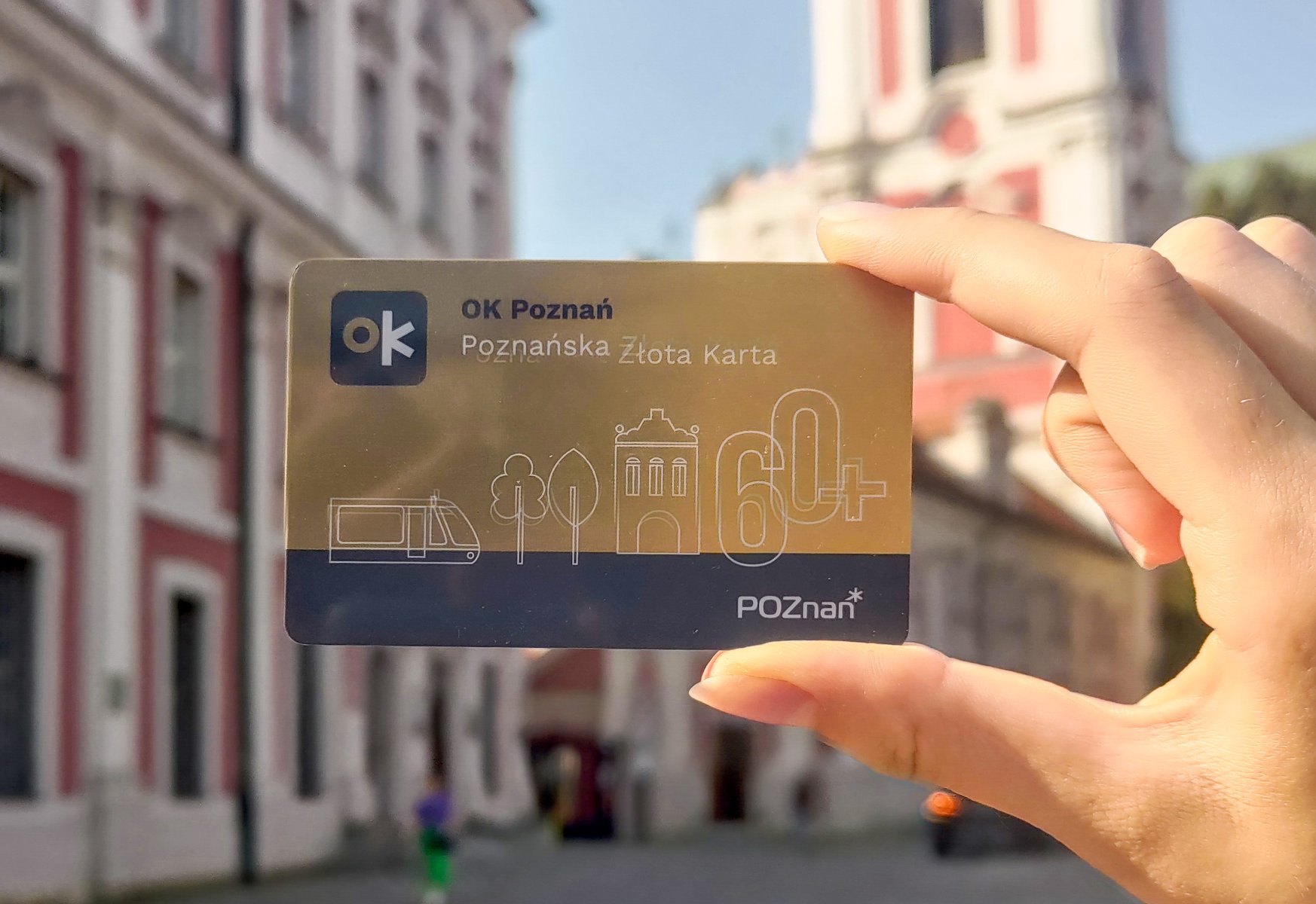 Na zdjęciu dłoń trzymająca kartę, w tle budynek urzędu miasta
