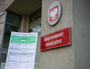 Na zdjęciu dłoń trzymająca zeznanie podatkowe, w tle urząd skarbowy