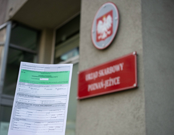 Na zdjęciu dłoń trzymająca zeznanie podatkowe, w tle urząd skarbowy