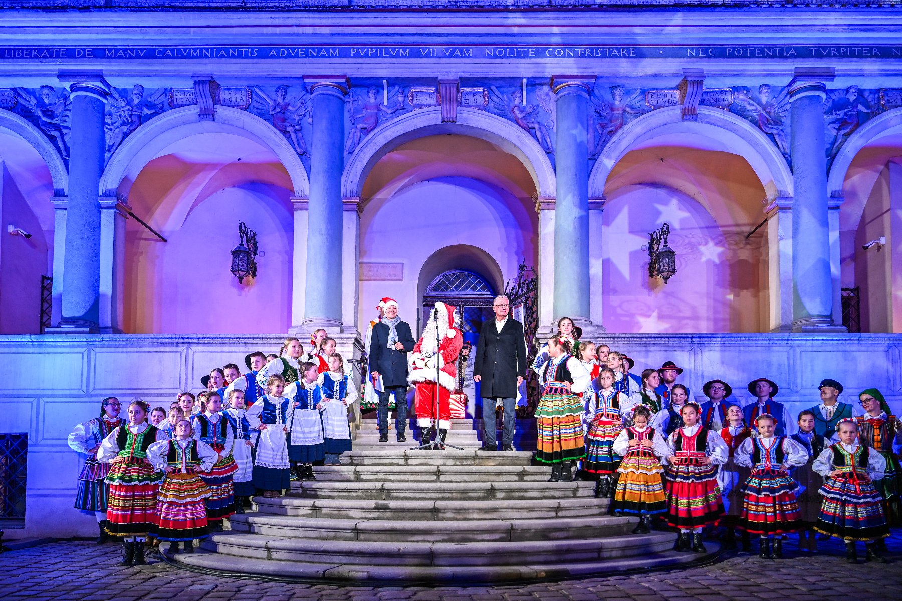 Na zdjęciu dużą choinka, przed nią ludzie, widać dwie duże pochodnie