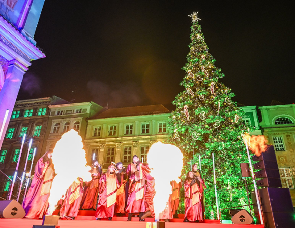 Na zdjęciu dużą choinka, przed nią ludzie, widać dwie duże pochodnie