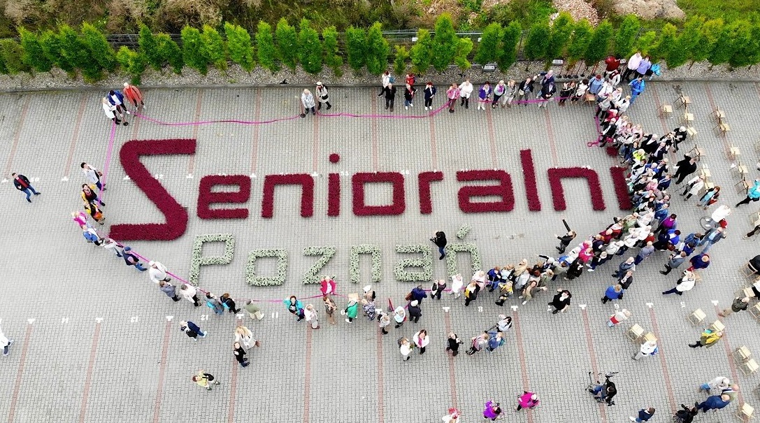 Na zdjęciu duży napis "Senioralni" ułożony z kwiatów, wokół niego widać ludzi