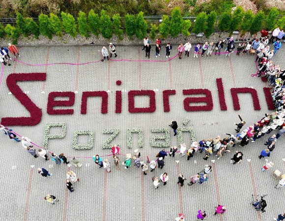 Na zdjęciu duży napis "Senioralni" ułożony z kwiatów, wokół niego widać ludzi