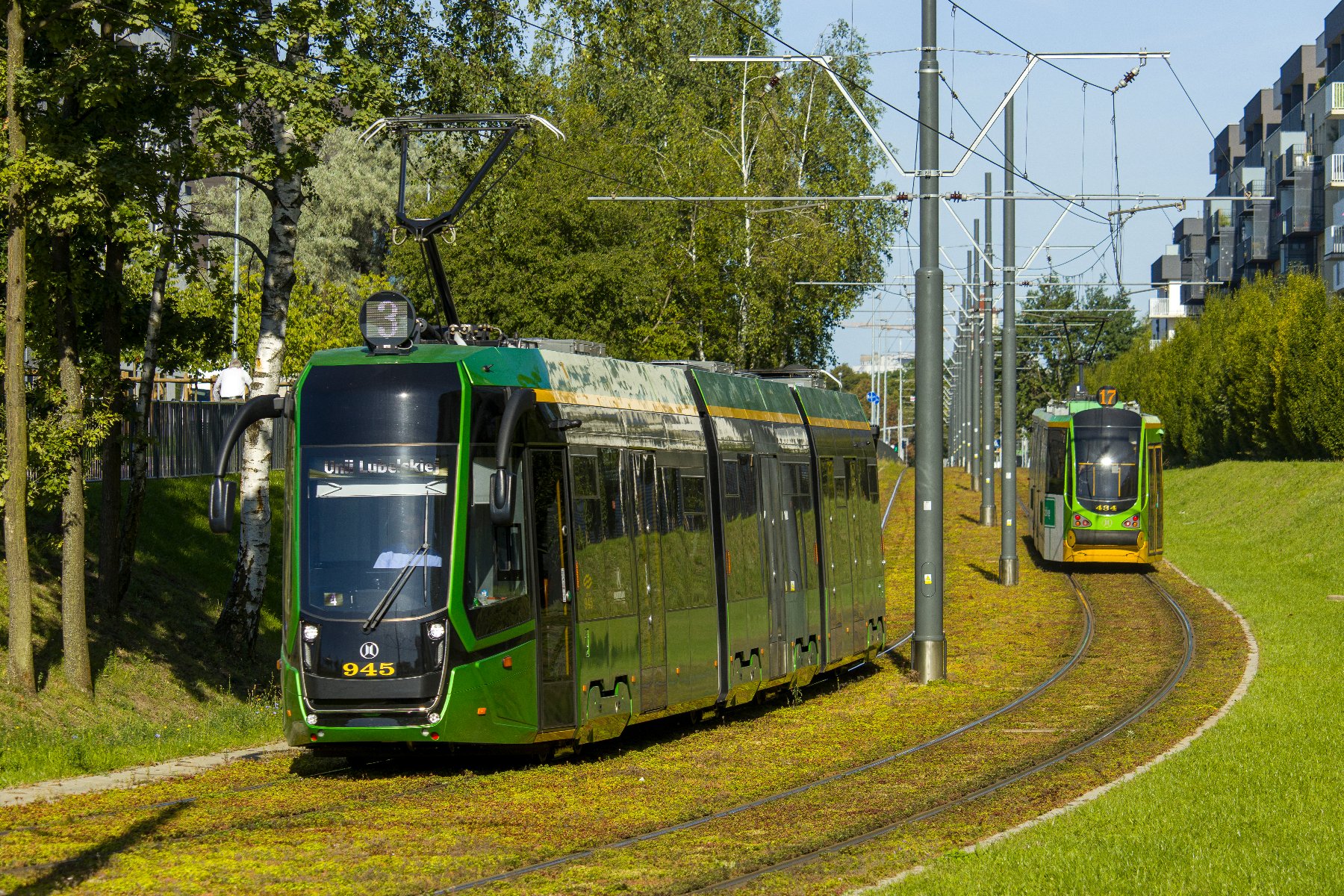 Na zdjeciu dwa tramwaje jadące przez zielone torowisko