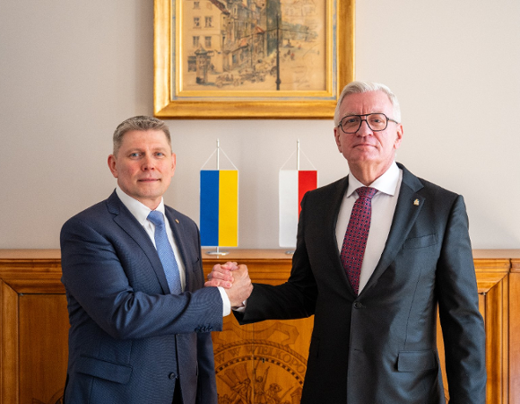 Na zdjęciu dwaj mężczyźni, podający sobie dłonie, w tle flagi Polski i Ukrainy