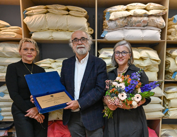 Na zdjęciu dwie kobiety i mężczyzna, jedna z kobiet trzyma kwiaty, mężczyzna - grawerton