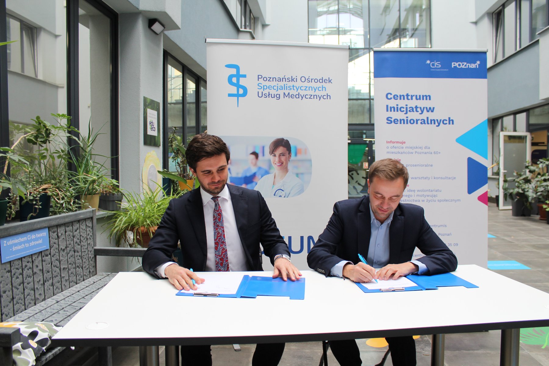 Na zdjęciu dwóch mężczyzn siedzących przy stoliku, podpisujących porozumienie