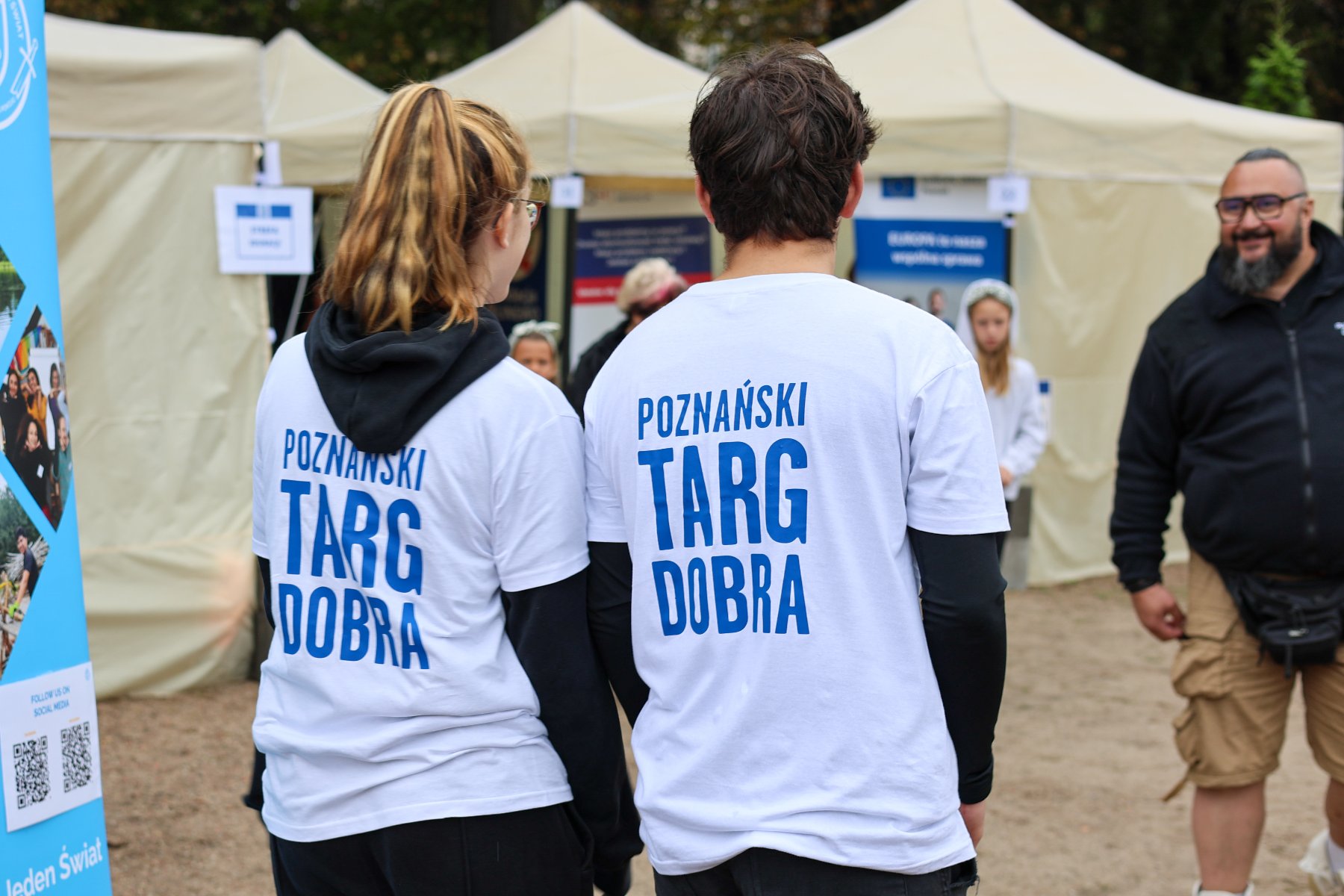 Na zdjęciu dwoje ludzi w koszulkach z napisem: Poznański Targ Dobra, w tle inni ludzie