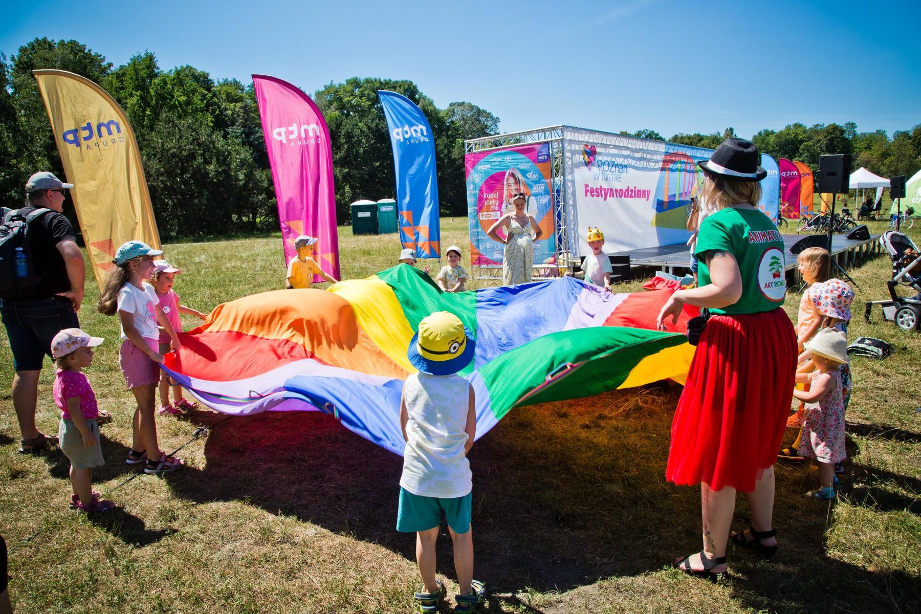 Na zdjęciu dzieci i animatorka bawiące się wielką, kolorową płachtą