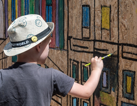 Na zdjęciu dziecko malujące poznańskie budynki na dużej dykcie