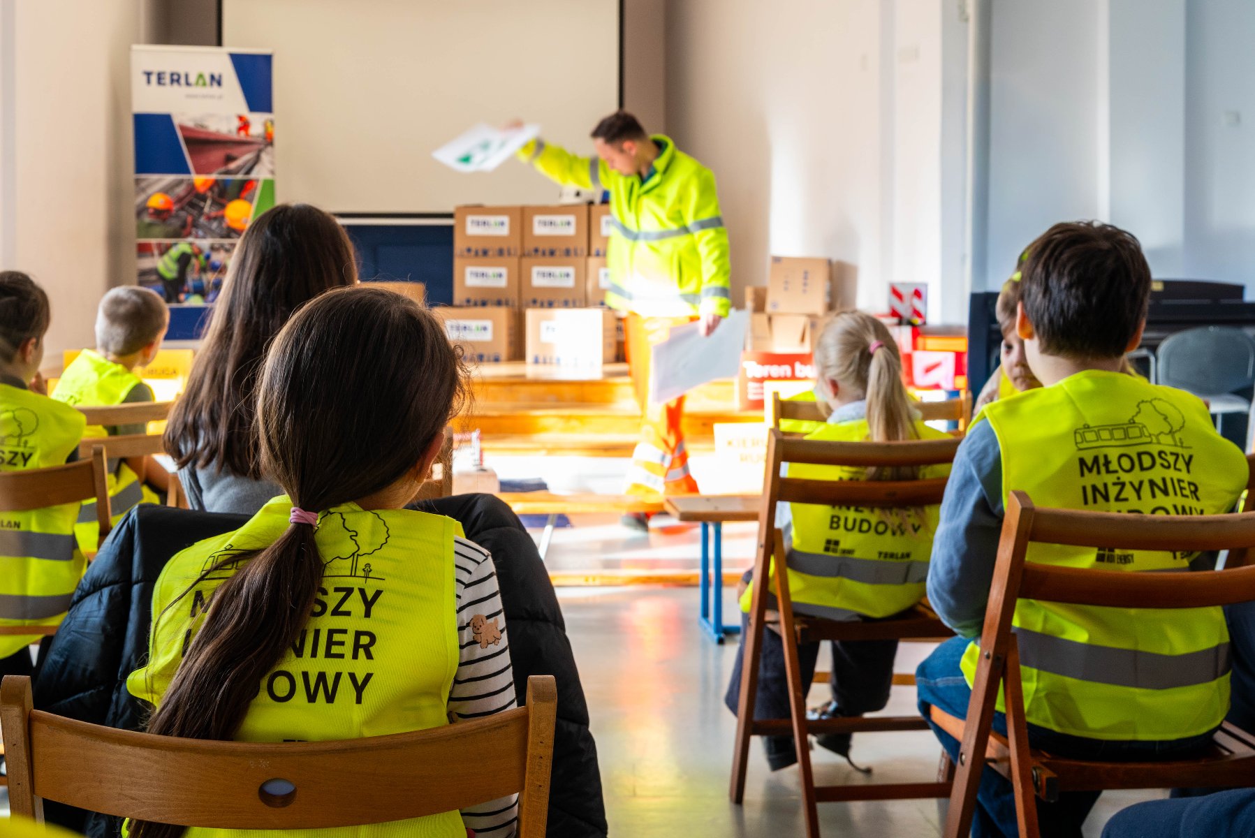 Na zdjeciu grupa dzieci w kamizelkach odblaskowych, przyglądają się czemuś