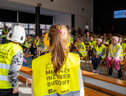 Na zdjeciu grupa dzieci w kamizelkach odblaskowych, przyglądają się czemuś