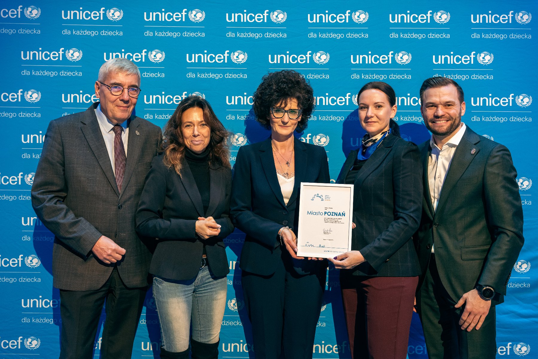 Na zdjęciu grupa ludzi pozująca do zdjęcia, w centrum dwie kobiety trzymają certyfikat