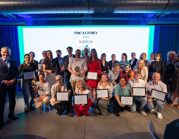Na zdjęciu grupa ludzi pozujących do obiektywu, w tle ekran, na nim napis: inicjatory 2024