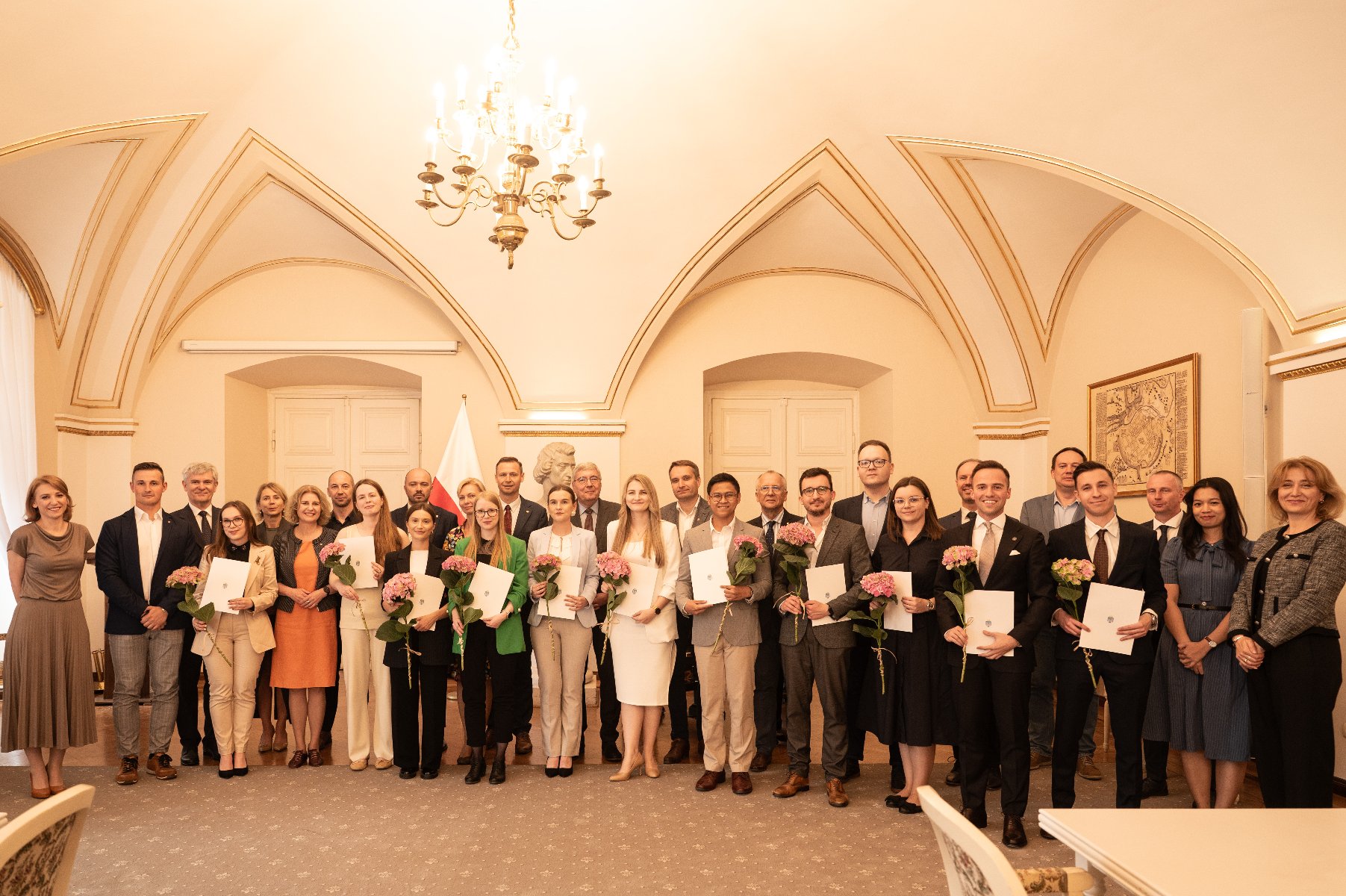na zdjęciu grupa osób trzymających dyplomy i kwiaty
