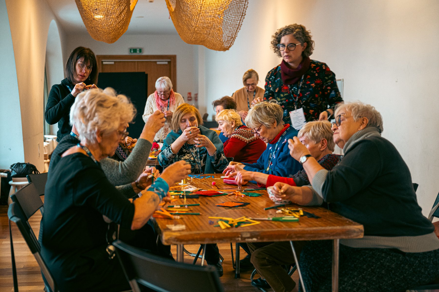 Na zdjęciu grupa seniorów przy stole, zajmują się rękodziełem