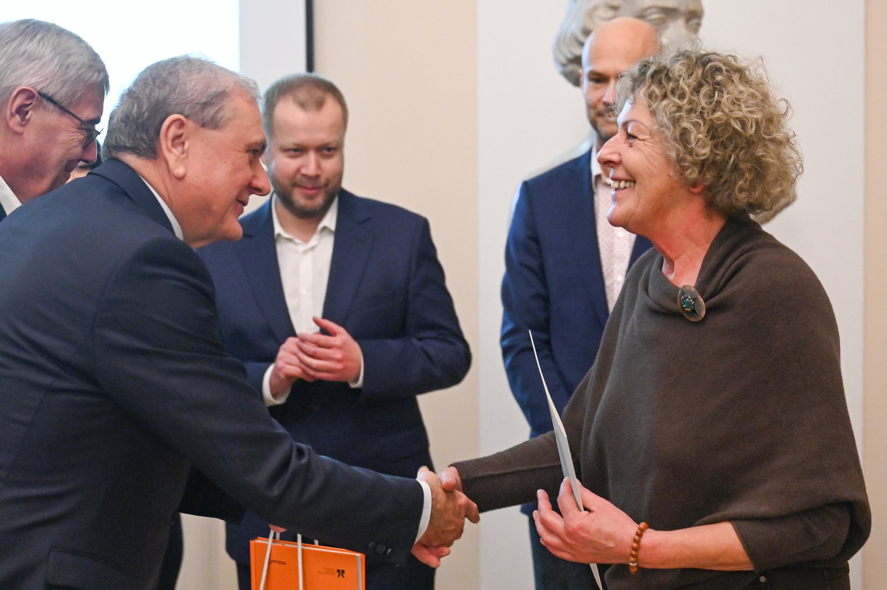 Na zdjęciu kilka osób, mężczyzna i kobieta podają sobie dłonie