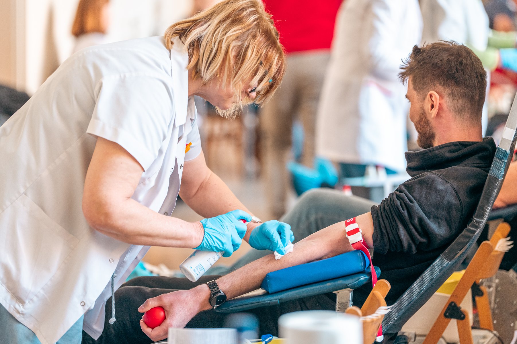 Na zdjęciu kilka osób na fotelach do oddawania krwi, na pierwszym planie ręka mężczyzny, trzymającego w dłoni czerwoną piłeczkę