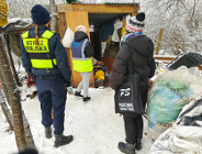 Na zdjeciu kilka osób, niektóre w kamizelkach odblaskowych, stoją przed szopą, w której schronienie ma osoba w kryzysie bezdomności