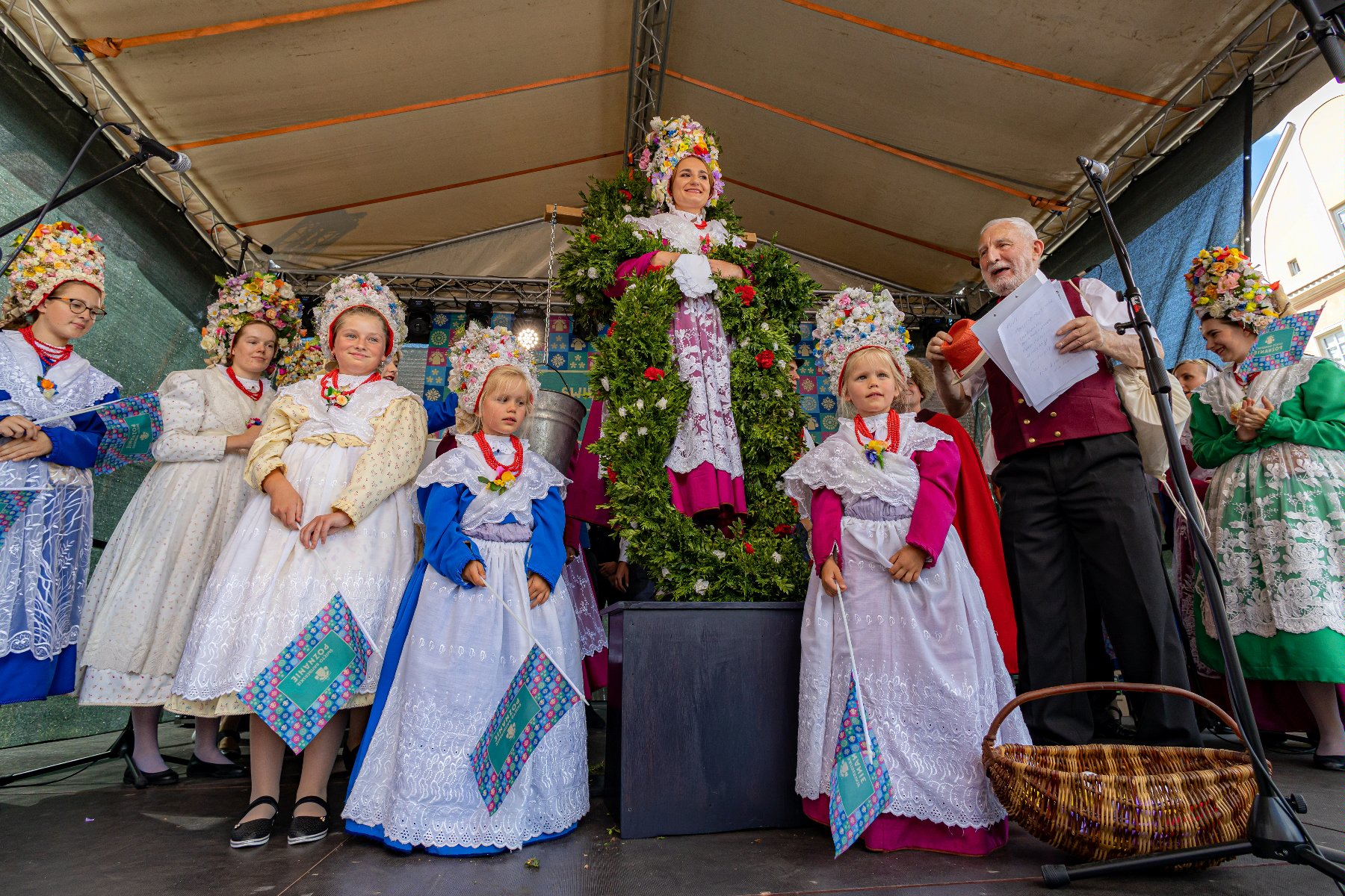 Na zdjęciu kilka osób w strojach Bambrów, w centrum kobieta z wiadrami wody i wieńcem na szyi
