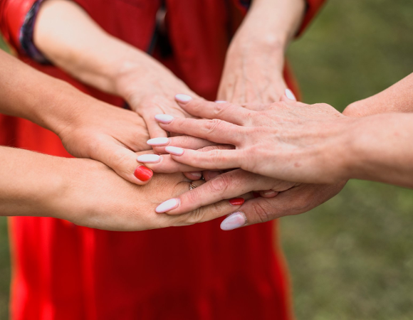 Na zdjęciu kobiece dłonie złożone razem we wspólnym geście, jedna na drugiej