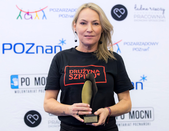 Na zdjęciu kobieta ieta trzymająca statuetkę na tle ścianki z logo miasta