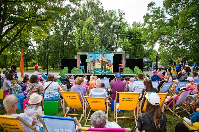 Na zdjeciu ludzie na leżakach rozstawionych w plenerze oglądają spektakl