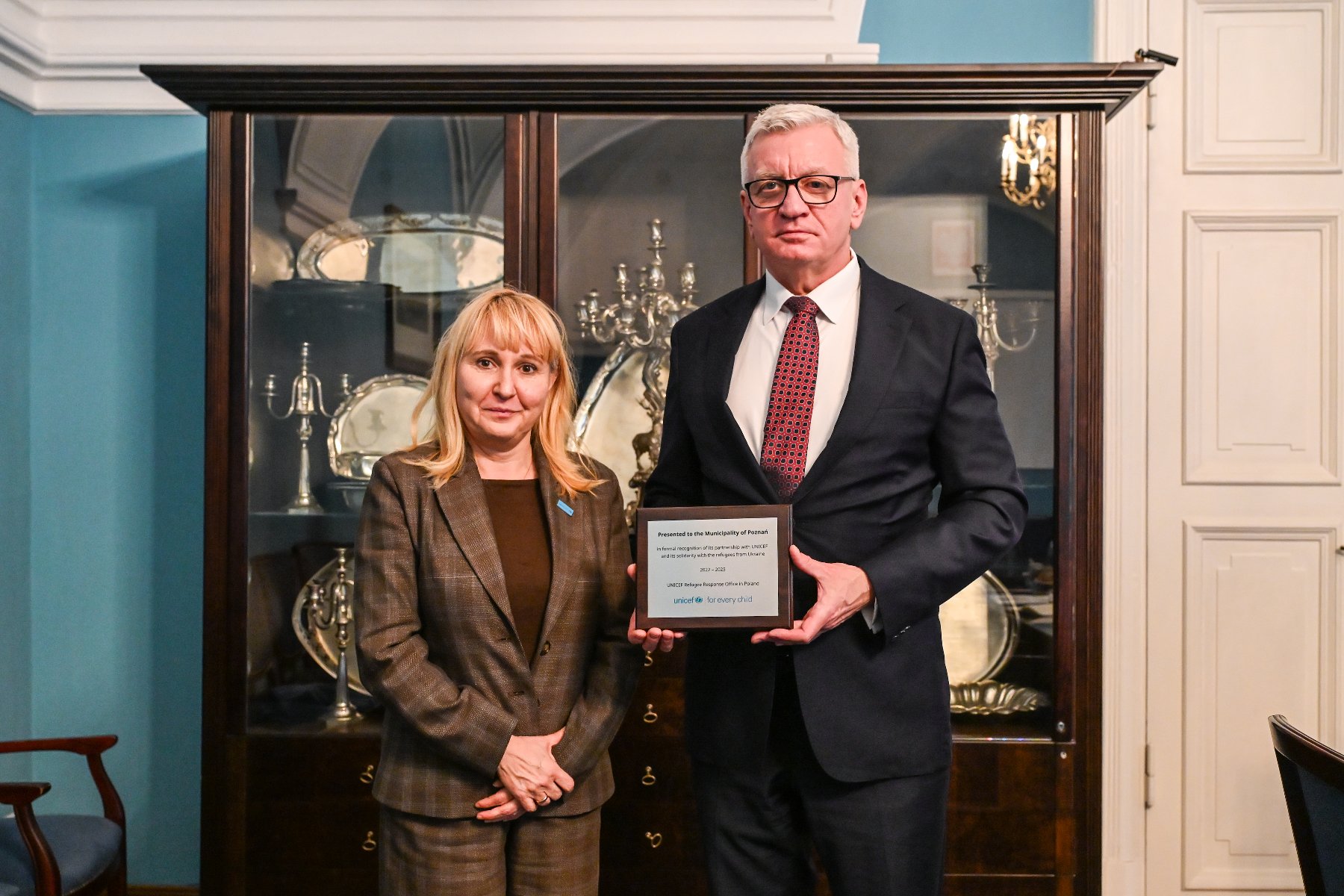 Na zdjęciu mężczyzna i kobieta pozują do obiektywu, mężczyzna trzyma tabliczkę