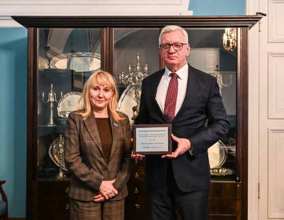 Na zdjęciu mężczyzna i kobieta pozują do obiektywu, mężczyzna trzyma tabliczkę