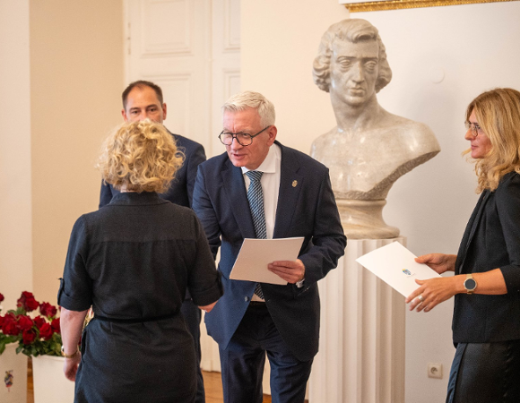 Na zdjęciu mężczyzna wręczający teczkę i kwiat kobiecie