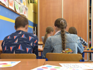 Na zdjęciu młodzi ludzie siedzący w szkolnej ławce, tyłem do obiektywu