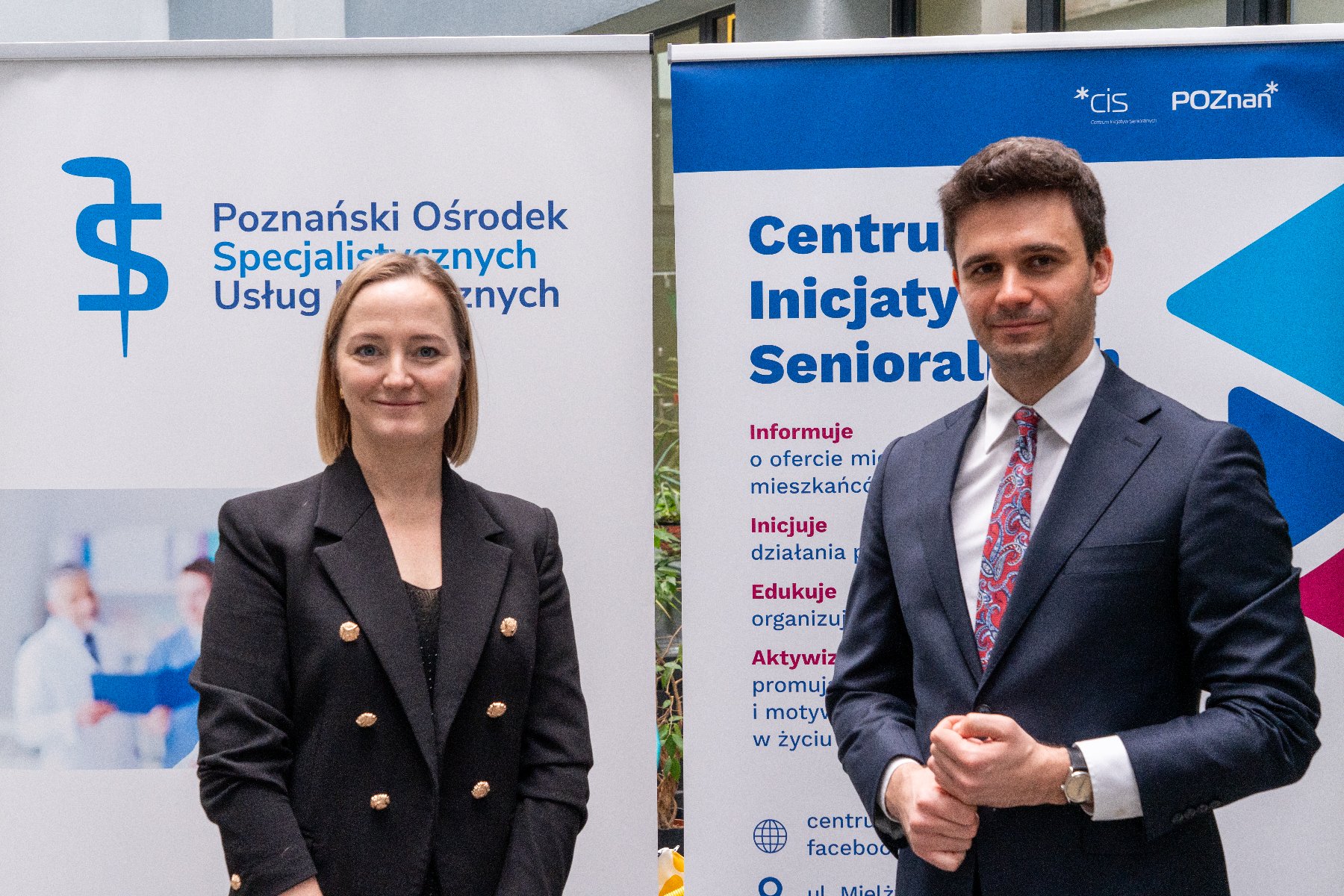 Na zdjęciu plakat zapowiadający akademię, w tle stoi kobieta, mówi coś do mikrofonu, za nią mężczyzna