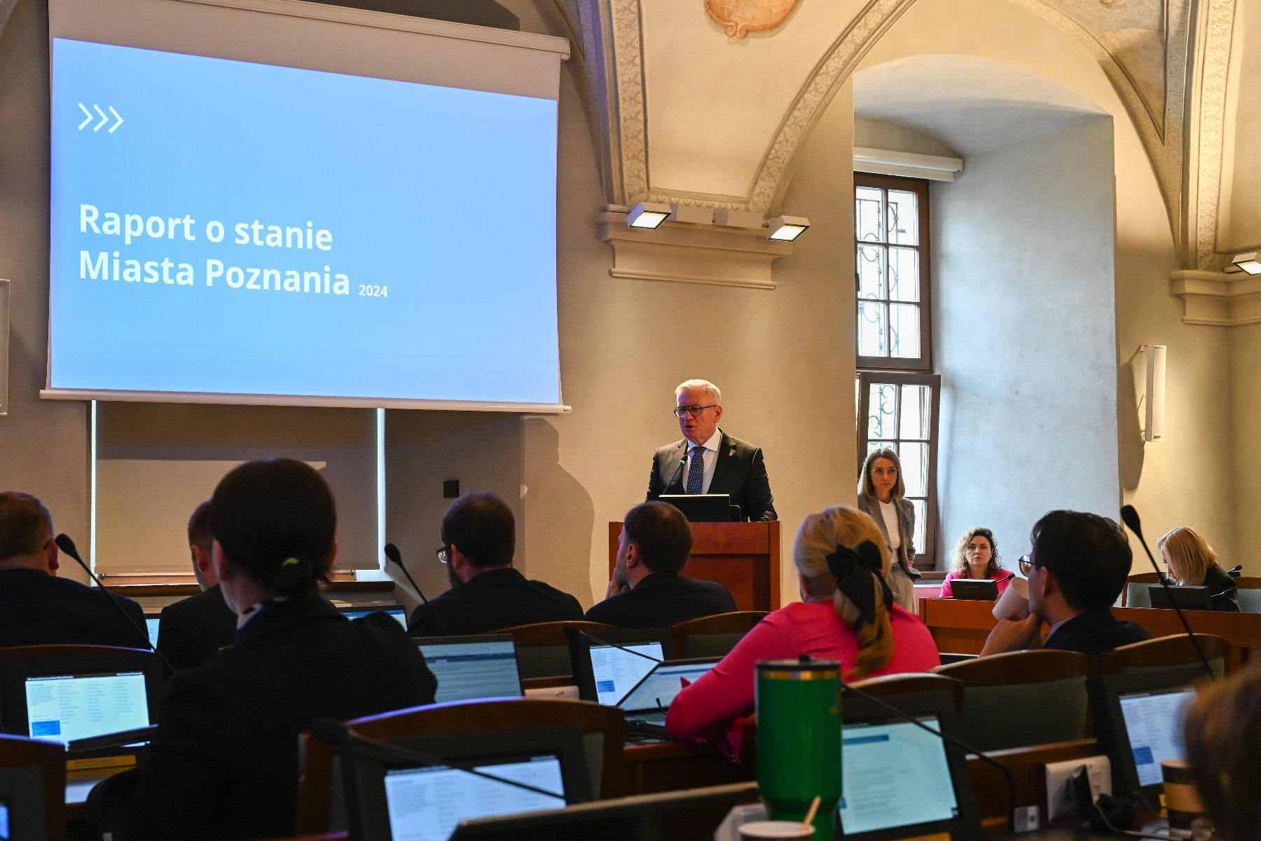 Na zdjeciu prezydent Poznania przy mównicy, obok ekran ze slajdem, na nim dane dotyczące gospodarki Poznania