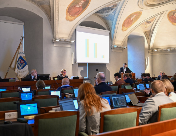Na zdjęciu sala sesyjna, w niej siedzą radni, przy mównicy stoi mężczyzna