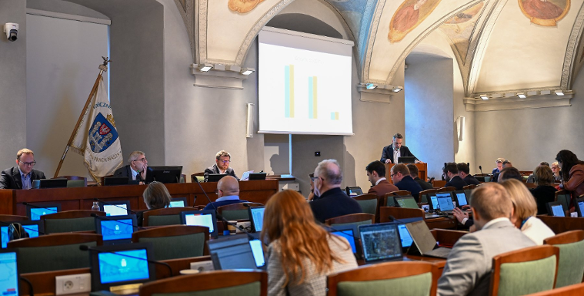 Na zdjęciu sala sesyjna, w niej siedzą radni, przy mównicy stoi mężczyzna